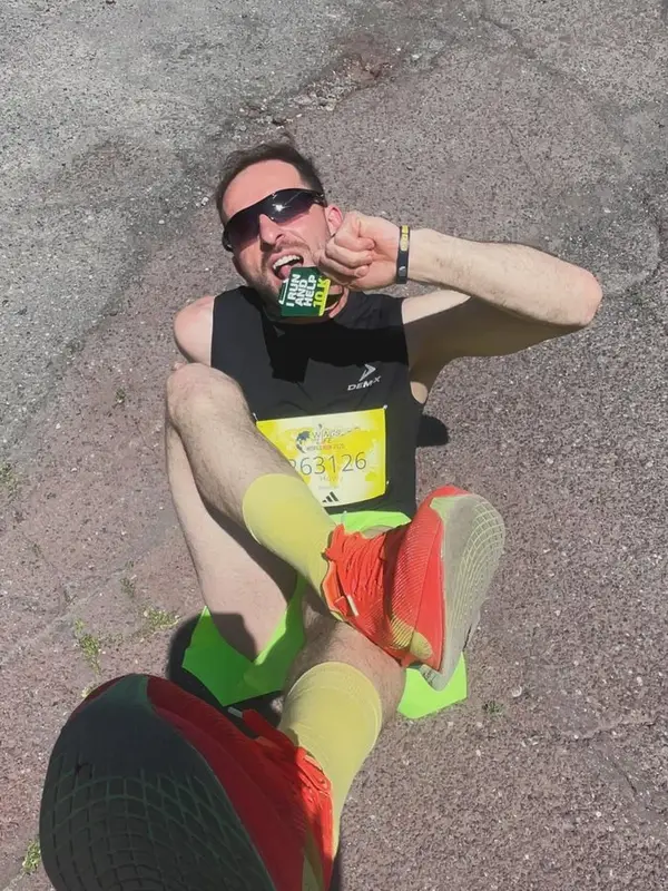 Har Hov sitting on the road after a race, biting his finisher medal
