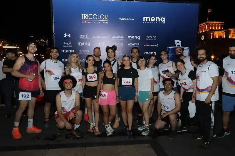 A large group in race bibs posing at a night race start